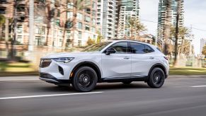 A 2021 Buick Envision driving on a highway with tall blurred buildings in the background.