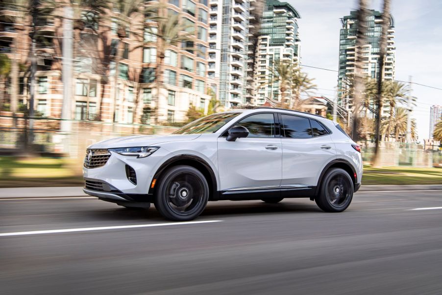 A 2021 Buick Envision driving on a highway with tall blurred buildings in the background.