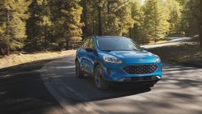 A teal 2021 Ford Escape Driving on a highway in a very wooded area.