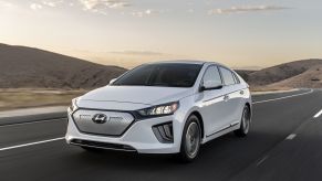 A white 2021 Hyundai Ioniq Electric sedan model driving on a highway