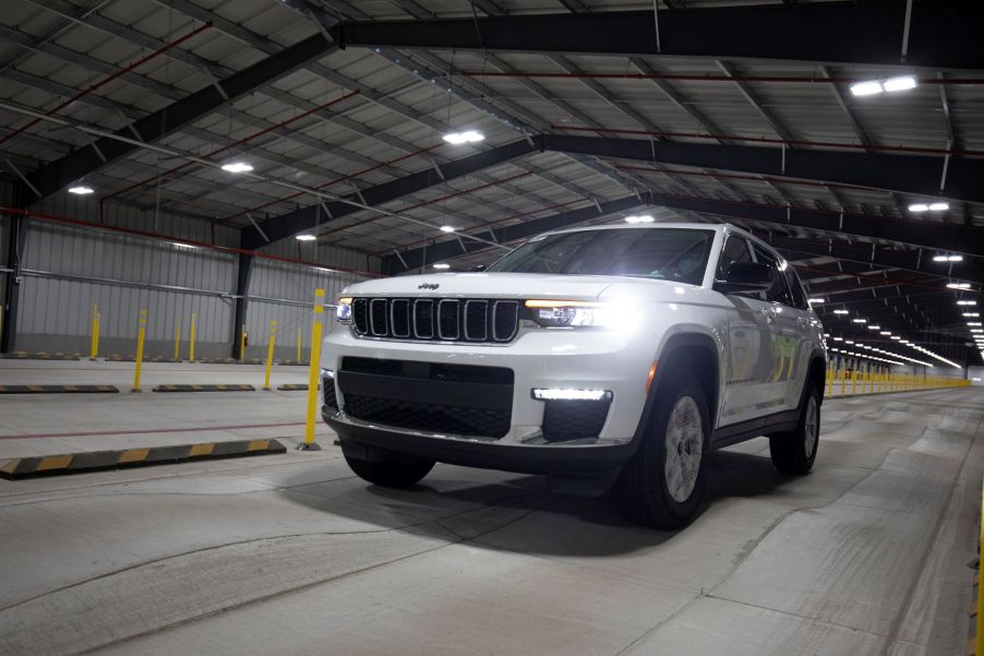 A white 2021 Jeep Grand Cherokee driving inside of a metal hanger building with a concrete floor.