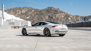 A white 2021 Karma GS-6 sports sedan parked outside a white warehouse in front of a mountain range on a sunny day