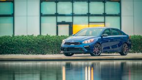 A blue 2021 Kia Forte GT Sport sedan model parked near a pond outside of a dealership