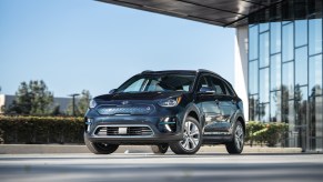 A dark-blue 2021 Kia Niro EV parked on concrete outside a modern glass building on a sunny day