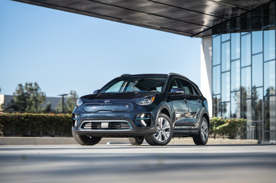 A dark-blue 2021 Kia Niro EV parked on concrete outside a modern glass building on a sunny day