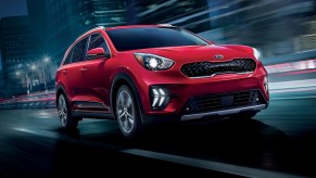 A red 2021 Kia Niro plug-in hybrid compact SUV traveling on a wet city street at night