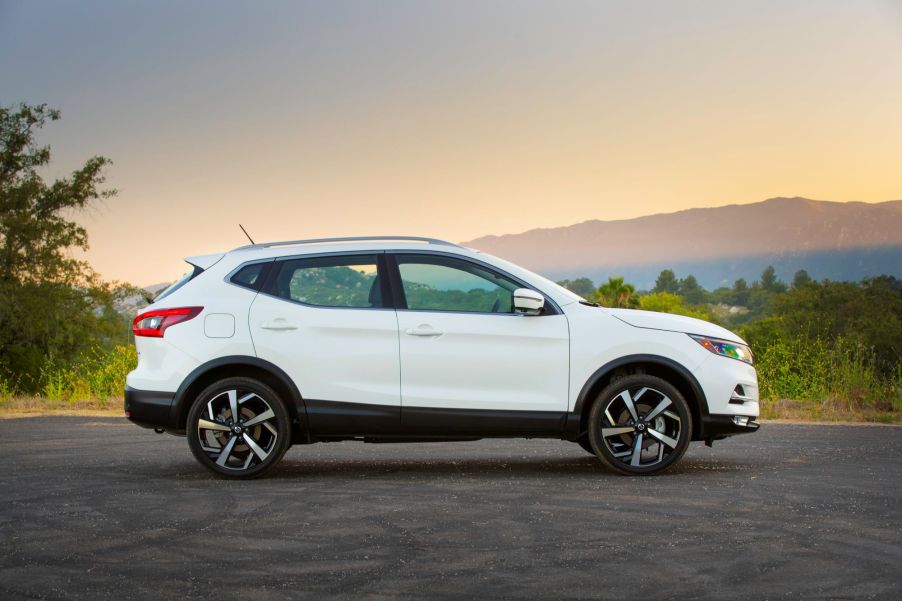 A white side-view of the 2021 Nissan Rogue on a blacktopped area with a background of a clear sunset with hills and trees.