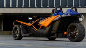 The rear 3/4 view of a blue-and-orange 2021 Polaris Slingshot R in a parking lot