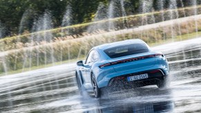 A sky-blue 2021 Porsche Taycan 4S maneuvers on wet pavement as water shoots into the air