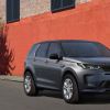 A grey 2021 Range Rover Evoque sits in front of a orange and grey brick building with two windows on a blacktop road.