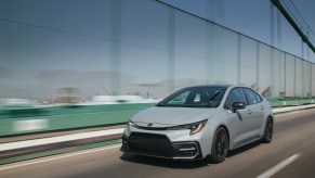 A gray 2021 Toyota Corolla Apex Edition compact car traveling on a bridge alongside a ship port