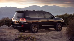 A 2021 Toyota Land Cruiser SUV parked on a rocky plain as the sun sets over a mountain range