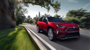 A red 2021 Toyota RAV4 Prime plug-in hybrid compact SUV traveling on a road away from a city