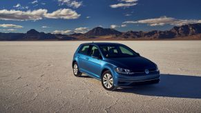 A blue 2021 Volkswagen Golf hatchback parked on a desert plain near a mountain range