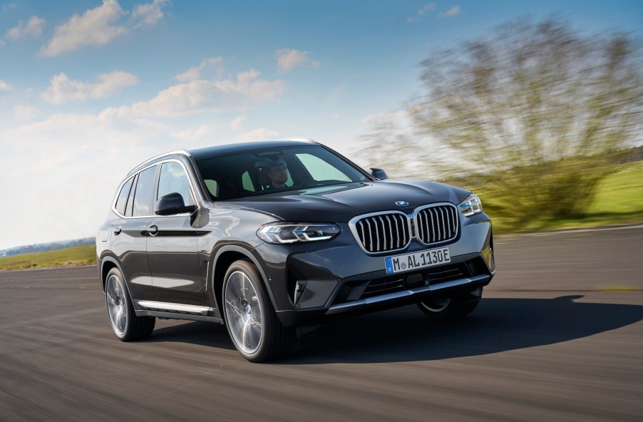 A dark-gray metallic 2022 BMW X3 xDrive30e luxury compact SUV travels on a country road along green hills