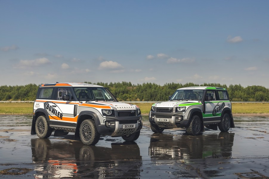 An orange-and-white and green-and-white 2022 Bowler Land Rover Defender 90 Challenge racer on a wet airstrip