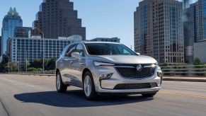 A silver 2022 Buick Enclave driving through a city surrounded by sky scrapers driving on a highway.