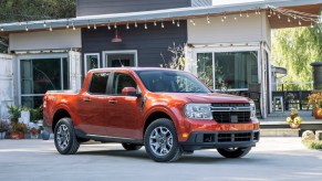 An orange 2022 Ford Maverick parked in front of a house with vintage bulb lights hanging above it, the 2022 Ford Maverick is a hybrid truck