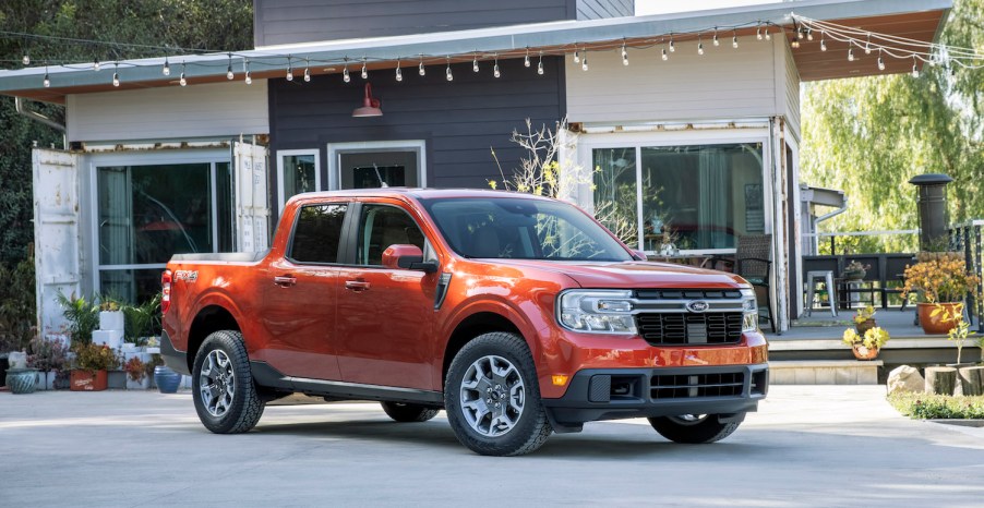 An orange 2022 Ford Maverick parked in front of a house with vintage bulb lights hanging above it, the 2022 Ford Maverick is a hybrid truck