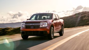 A red 2022 Ford Maverick Lariat driving down a highway with green rolling hills in the background