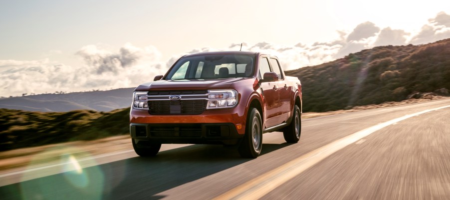 A red 2022 Ford Maverick Lariat driving down a highway with green rolling hills in the background