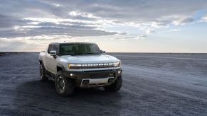 A white 2022 GMC Hummer EV sitting on flat dirt with a cloudy sunset behind it.