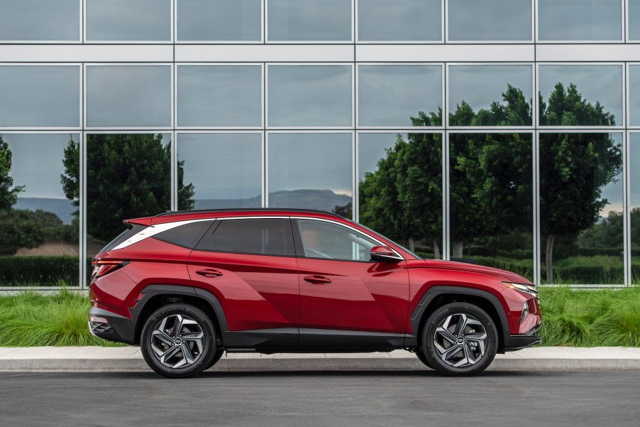 A cherry-red metallic 2022 Hyundai Tucson parked on the street outside a glass building