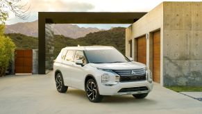 A white 2022 Mitsubishi Outlander SUV parked out of a luxury home in the mountains