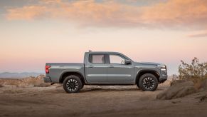 A Silver Nissan Frontier in a desert area with a slightly cloudy sunset colored sky in the background.