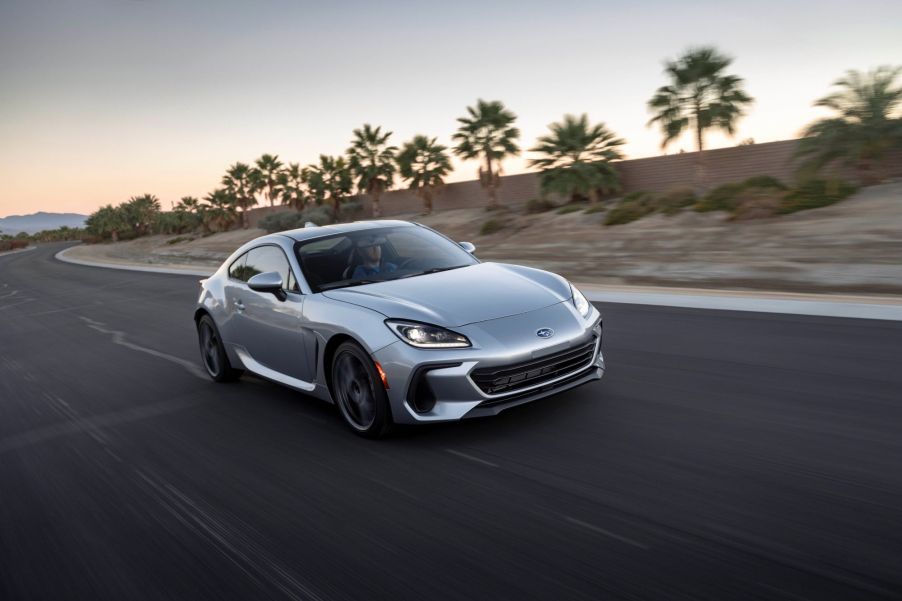 A silver 2022 Subaru BRZ driving down a road in a desert tropical area with sand and palm trees.