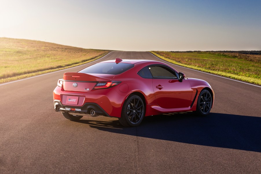 A red 2022 Toyota GR 86 sports car parked on a strip of asphalt running through rolling green hills on a sunny day