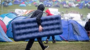 A man carrying an air mattress into a festival as it rains