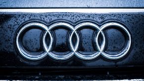 Audi's logo of the four connected rings are placed on a black background of a car grille with raindrops.