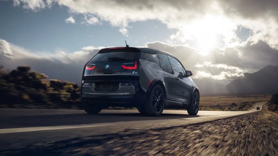 The 2021 BMW i3 drives away on a road surrounded by farmland.