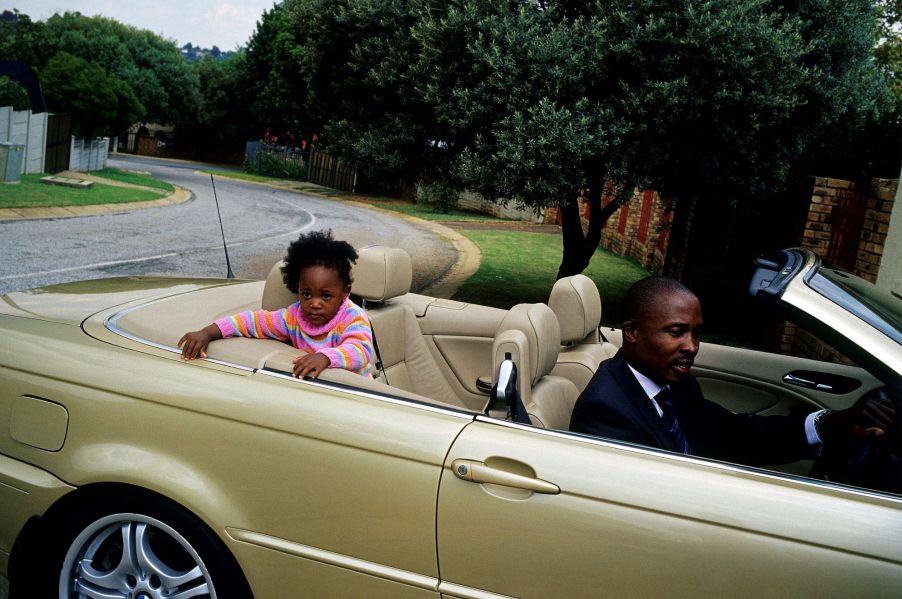 A father driving a gold convertible with his daughter in the back seat