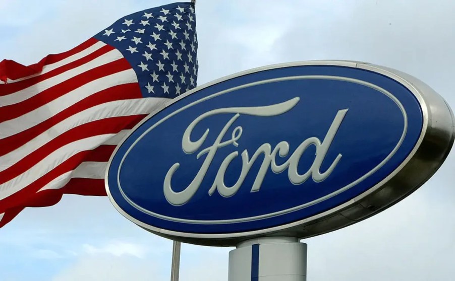 A Ford sign at a dealership next to a flying flag.