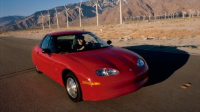 A red GM EV1 parked on a road alongside wind turbines and mountains