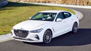 A white Genesis G70 luxury sedan model driving on a country highway