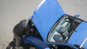 A man peers under the hood of a car that won't start