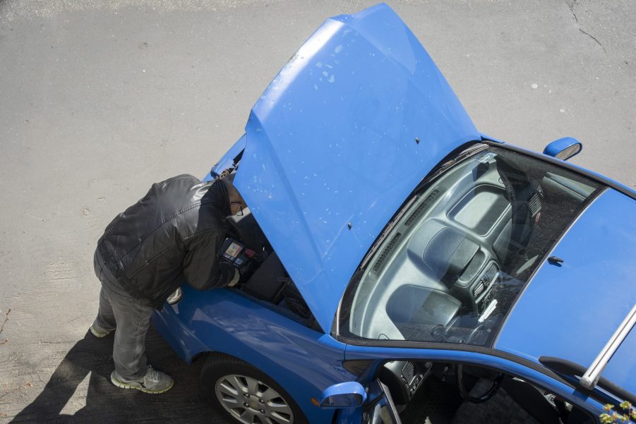 A man peers under the hood of a car that won't start