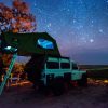 A Land Rover with a roof tent parked under the stars