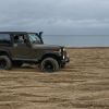 A Jeep Wrangler military model driving on a Baltic Sea coast beach