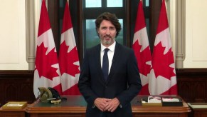 Justin Trudeau speaks in front of four Canadian flags.