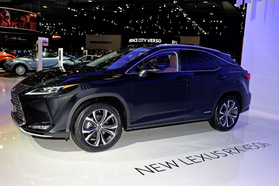 A dark blue Lexus RX sitting in a showroom with other cars behind it on a white floor with black lettering stating "New Lexus RX 450h" on the floor.