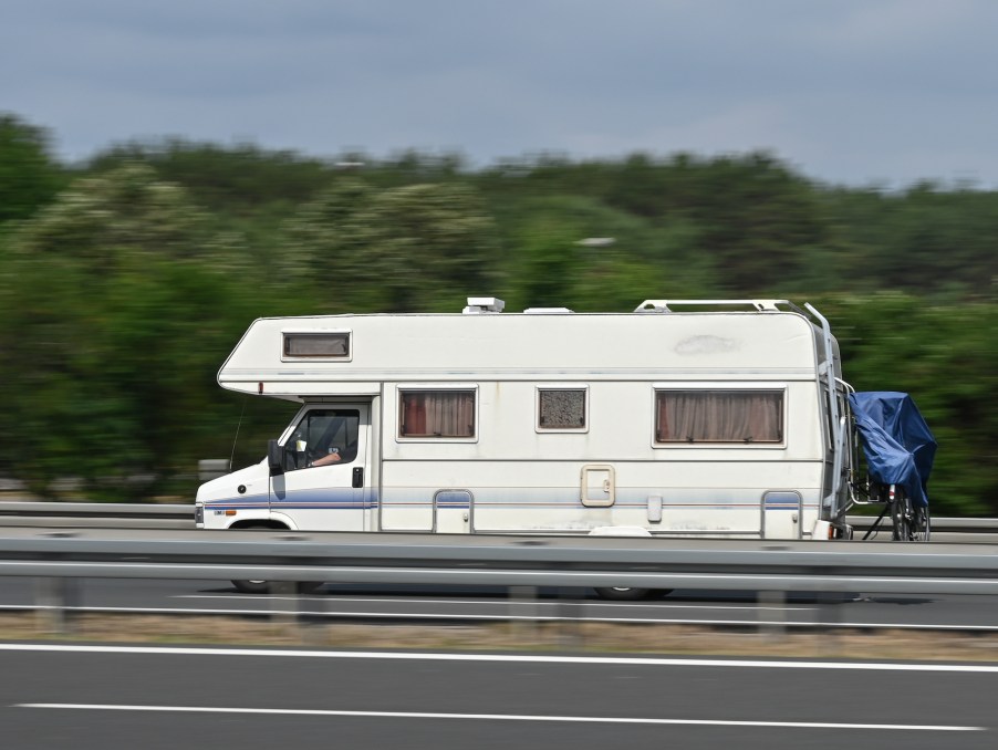 An RV travels on a road along a guardrail and trees