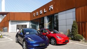 A pair of blue and red Tesla models parked outside of a Tesla showroom building