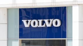 A large blue sign with 'Volvo' printed framed by a white section of what looks like a building with a glass window underneath the sign.