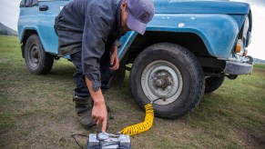 A man turns on a battery-powered air compressor whose hose is attached to his SUV's right front tire