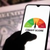 A photo illustration of a hand holding a smartphone showing a graph with the credit score