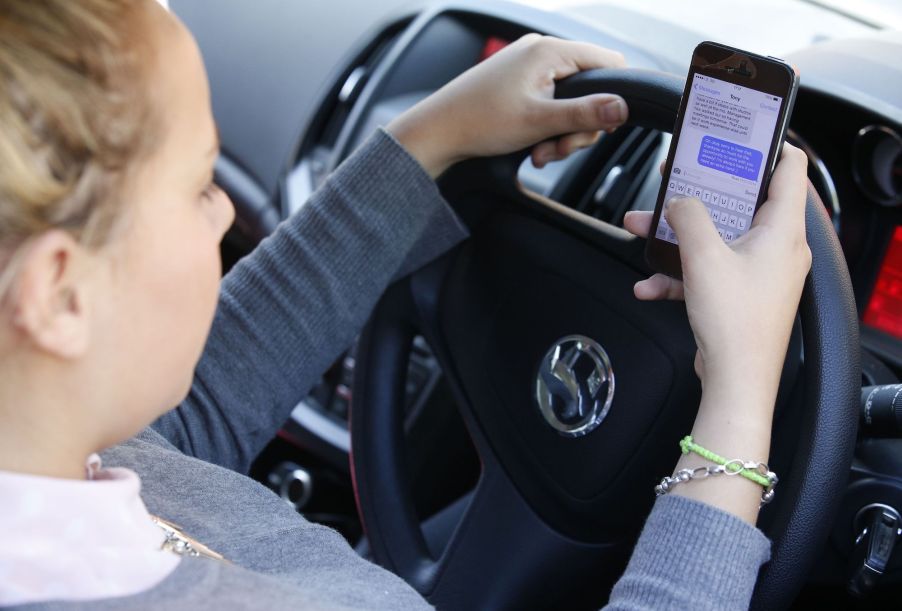 A young woman texts on her phone while driving, the biggest driving distraction